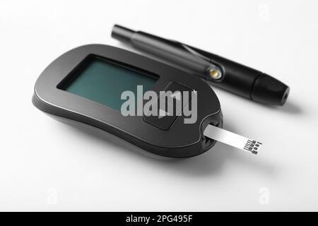 Glucometro digitale con striscia reattiva e penna a lancetta su sfondo bianco. Controllo del diabete Foto Stock