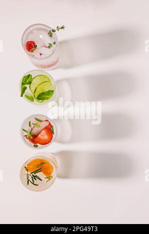 Vista dall'alto di bicchieri a coste con limonata o acqua infusa con sapori diversi sul tavolo bianco Foto Stock