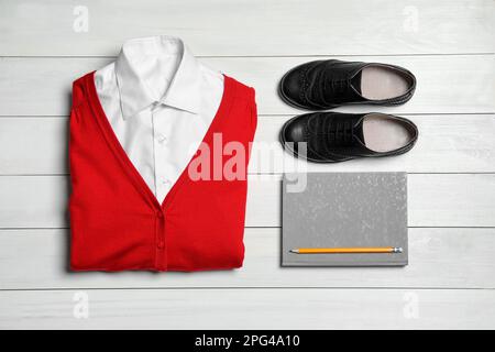 Scuola elegante per ragazza uniforme e notebook su sfondo bianco in legno, piatto Foto Stock