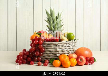 Cestino di vimini con frutta fresca diversa su un tavolo di legno bianco Foto Stock