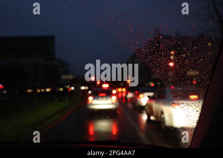 Vista offuscata della strada attraverso il finestrino dell'auto bagnata di notte. Effetto bokeh Foto Stock