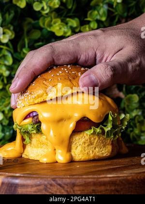 Primo piano di una mano umana che tiene un cheeseburger appena fatto, completo di lattuga e salsa Foto Stock