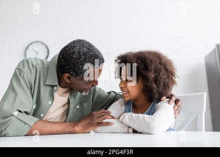 felice nonno afroamericano abbracciando la nipote ricciolo in cucina, immagine di scorta Foto Stock