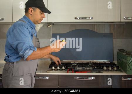 Immagine di un tecnico di handyman che con un rilevatore effettua controlli in cucina per la sicurezza e le perdite di gas dalla stufa. Prevenzione e sicurezza Foto Stock