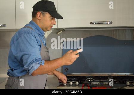 Immagine di un tecnico di handyman che con un rilevatore effettua controlli in cucina per la sicurezza e le perdite di gas dalla stufa. Prevenzione e sicurezza Foto Stock