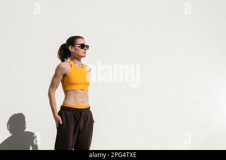 Donna in forma, sportiva e tonica che indossa un reggiseno sportivo, una tuta e un paio di occhiali da sole. Foto Stock