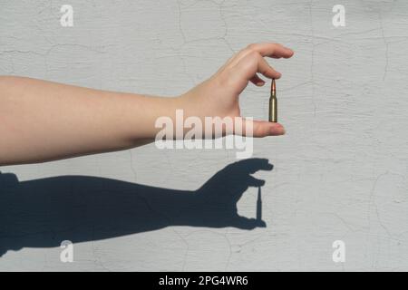 Cartuccia del fucile in mano contro lo sfondo di una parete bianca in cemento. Sulla parete si forma un'ombra Foto Stock