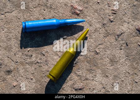 Le cartucce di fucile giallo e blu (simbolo nazionale dell'Ucraina) giacciono su una superficie di cemento (primo piano). Il concetto di sostegno militare all'Ucraina Foto Stock