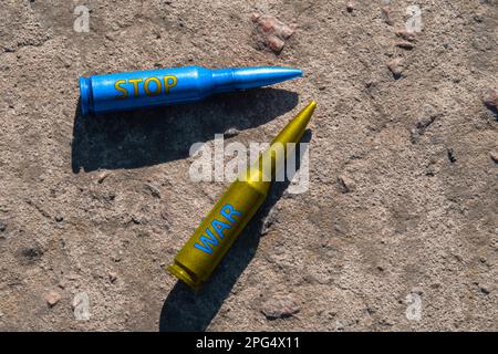 Le cartucce del fucile giallo e blu con l'iscrizione STOP WAR giacciono su una superficie di cemento (primo piano). Il concetto di sostegno militare all'Ucraina Foto Stock