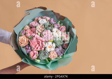 L'uomo senza volto tiene in mano un bouquet di fiori dolci di marshmallow. Confezione regalo in verde pastello con delicate rose senza zucchero su fondo arancione. SMA Foto Stock