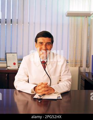 Medico maschio seduto alla sua scrivania in una sala di consulenza. Foto Stock
