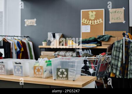 Parte di spazioso deposito o ufficio di organizzazione di volontariato con scatole di plastica per diversi tipi di rifiuti e vestiti di seconda mano Foto Stock