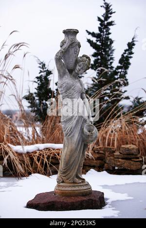 Una splendida scena invernale all'aperto caratterizzata da una statua ricoperta di neve sullo sfondo di erba verde e arbusti contrastanti. Foto Stock