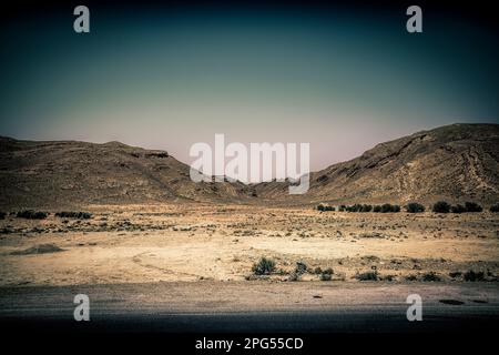 Immergiti nella bellezza mozzafiato del paesaggio desertico della Tunisia, con due torreggianti colline e una tranquilla valle immersa in un blu chiaro Foto Stock