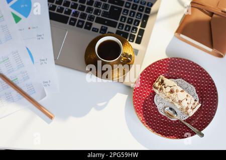 Concetto di salute mentale sul lavoro. Vista superiore del tavolo in un ufficio moderno con pezzo di torta, tazza di caffè, documenti e computer portatile. Foto Stock
