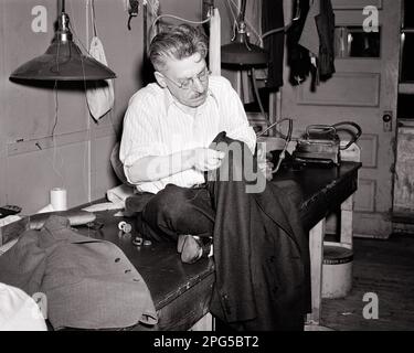 1940S UOMO DI MEZZA ETÀ UN SARTO SEDUTO IN CIMA AD UN BANCONE IN UN NEGOZIO CUCENDO UNA GIACCA TUTA UOMO - C2028 HAR001 HARS PROFESSIONE MESTIERE DI MEZZA ETÀ B&W UOMO DI MEZZA ETÀ ABILITÀ PROFESSIONE COMPETENZE SERVIZIO CLIENTI CUSTOM CARRIERE OCCUPAZIONI MESTIERI UOMO MESTIERE UOMO NERO E BIANCO ETNICITÀ CAUCASICA HAR001 VECCHIO STILE Foto Stock