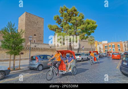 BARI, ITALIA - 26 settembre 2019 Rickshaws passando per il castello svevo o Castello Svevo, un punto di riferimento medievale della Puglia nel centro della città. Foto Stock