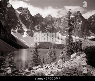 1960S UN UOMO IN PIEDI SULLA COLLINA PRESSO IL LAGO MORAINE NELLA CANADIAN ROCKIES VALLEY DEL PARCO NAZIONALE DI TEN PEAKS BANFF ALBERTA CANADA - M8313 HAR001 HARS SPIRITUALITÀ ESCURSIONE B&W NORD AMERICA LIBERTÀ NORD AMERICA ALTA ANGOLO AVVENTURA SCOPERTA CANADESE ESCURSIONISTA PARCHI ROCKIES ROCCE LONE MORAINE PEAKS NATIONAL PARK PANORAMICO VISTA ALBERTA COLLINA LAGHI METÀ-ADULTO UOMO METÀ-ADULTO DONNA PARCO NAZIONALE SERVICE BANFF NERO E BIANCO ETNICITÀ CAUCASICA FIR HAR001 MONTAGNOSO VECCHIO STILE Foto Stock