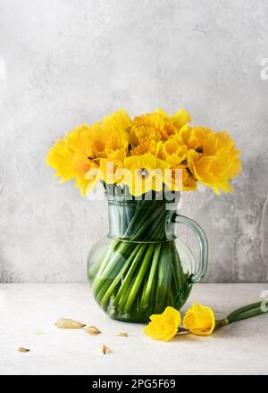 Vita morta con fiori gialli di daffodil in una caraffa di vetro vintage. Decorazione fatta in casa per Pasqua o il giorno della madri. Spazio di copia. Foto Stock