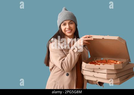 Giovane donna in cappello con scatole di gustosa pizza su sfondo blu Foto Stock