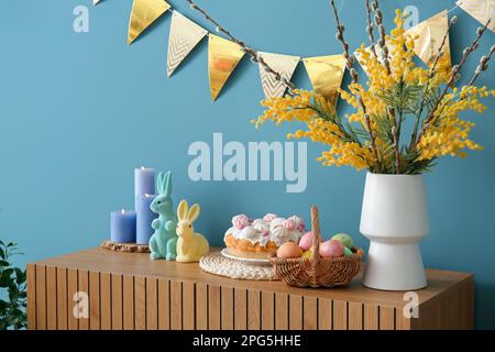 Decorazioni pasquali su armadio in legno vicino alle pareti blu Foto Stock