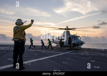 MARE DELLA CINA DEL SUD (16 marzo 2023) – Aviation Boatswain’s Mate (Handling) 3rd Classe Kejuan Holland, a sinistra, dirige i marinai dopo aver fissato i cunei e le catene su una UH-1Y Venom, assegnata a Marine Medium Tiltrotor Squadron (VMM) 362 (Rein.), 13th Marine Expeditionary Unit (MEU), Durante le operazioni di volo a bordo del molo di trasporto anfibio USS Anchorage (LPD 23), 16 marzo 2023. La sincronizzazione delle capacità complementari dell'Anchorage 13th MEU e USS moltiplica l'influenza tradizionale dell'energia marina per produrre una forza più competitiva e letale. Il Makin Island Anfibio Ready Group, compri Foto Stock