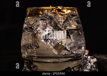Spruzzi d'acqua in una tazza di vetro da un cubo di ghiaccio rovesciato Foto Stock
