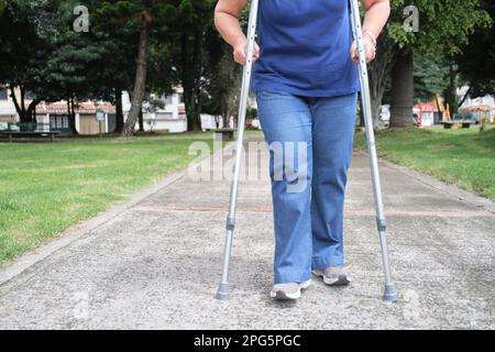 Persona irriconoscibile che cammina verso la macchina fotografica con l'aiuto di stampelle. Concetti: Mobilità ridotta, recupero e riabilitazione fisica dopo un Foto Stock