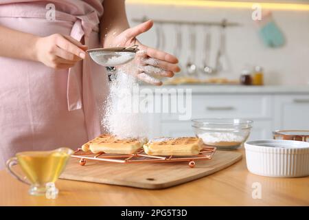 Donna decorazione deliziosi waffle belgi con zucchero a velo al tavolo in legno in cucina, primo piano Foto Stock