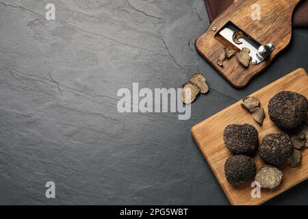 Rasoio in legno con tartufi interi e tagliati su tavolo nero, piatto. Spazio per il testo Foto Stock