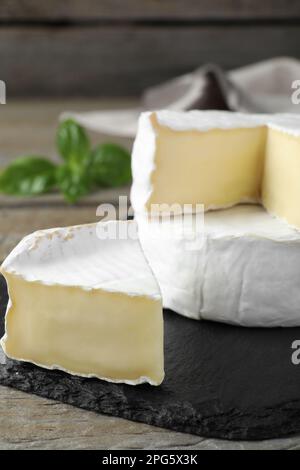 Gustosi formaggi brie tagliati e interi su tavola nera, primo piano Foto Stock