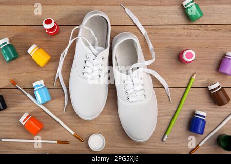 Sneakers bianche e forniture di pittura su tavolo di legno, piatto. Scarpe personalizzate Foto Stock