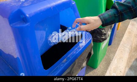 La gente lancia a mano una bottiglia d'acqua vuota nel cestino. Cestino in plastica blu. Uomo gettare la bottiglia d'acqua nel cestino. Gestione dei rifiuti. Plastica Foto Stock