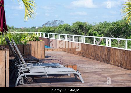 Terrazza esterna con pavimenti in legno e sedie da sole in un lussureggiante ambiente tropicale. Concetto di relax Haven Foto Stock