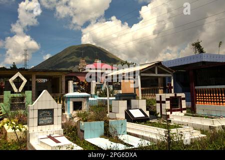 Un cimitero rurale sullo sfondo del Monte Lokon, un vulcano attivo a Tomohon, Sulawesi settentrionale, Indonesia. Foto Stock