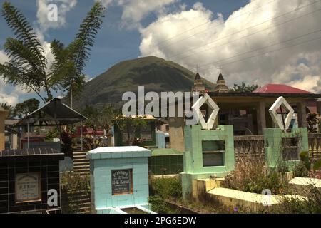 Un cimitero rurale sullo sfondo del Monte Lokon, un vulcano attivo a Tomohon, Sulawesi settentrionale, Indonesia. Foto Stock