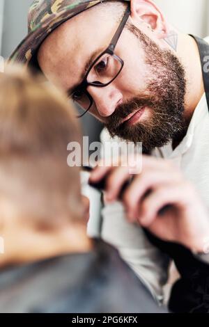 HES è sempre stato un perfezionista. un bel giovane barbiere che dona a un ragazzino un taglio di capelli all'interno di un barbiere. Foto Stock