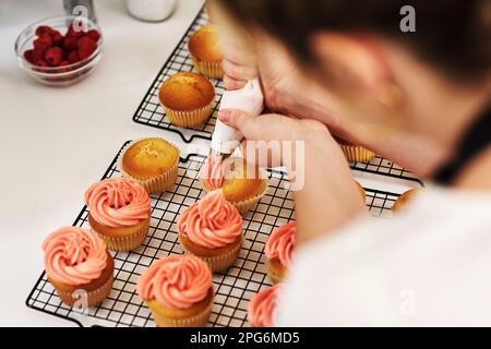 Hanno un sapore ancora migliore di quello che sembrano. una donna irriconoscibile che incamera la glassa sui suoi cupcakes. Foto Stock