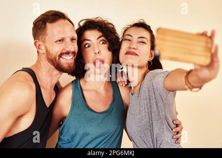 Il divertimento elimina l'allenamento. un gruppo di giovani uomini e donne che prendono selfie in classe yoga. Foto Stock