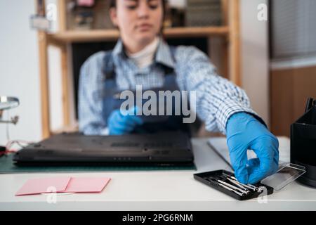 Tecnico che ripara il computer portatile rotto con un cacciavite. Svitando le viti dalla custodia del computer portatile con un cacciavite per la riparazione Foto Stock