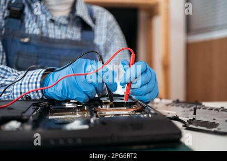 Concetto di servizio di riparazione dei notebook. Il multimetro per l'elettronica è in possesso delle mani Foto Stock