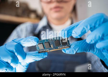 Tecnico dell'assistenza con memoria sulla scheda madre di un computer. RAM in mano sullo sfondo dell'officina di riparazione. Aggiornamento del personal computer Foto Stock