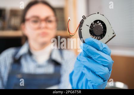 Officina di riparazione elettronica, ristrutturazione tecnologica, business, concetto di occupazione. Un riparatore disassemblando il computer portatile e tenendo la ventola in mano. Foto Stock