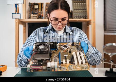 Un giovane riparatore smontando le parti interne di un computer nel centro di assistenza. Ingegnere informatico che lavora su una vecchia scheda madre. Foto Stock
