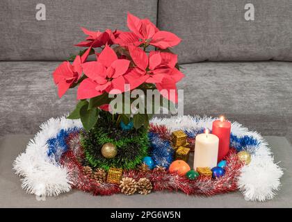 Inverno Natale decorazione tavolo vacanza con una poinsettia rosso brillante e ornamenti tradizionali con tinsel e due candele brucianti Foto Stock
