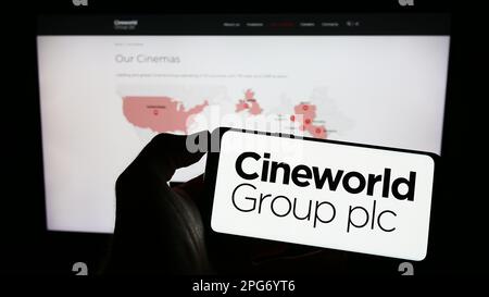 Persona che tiene uno smartphone con il logo della società cinematografica britannica Cineworld Group plc sullo schermo di fronte al sito Web. Messa a fuoco sul display del telefono. Foto Stock