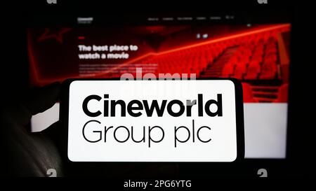 Persona che tiene il cellulare con il logo della società cinematografica britannica Cineworld Group plc sullo schermo di fronte al sito web aziendale. Messa a fuoco sul display del telefono. Foto Stock