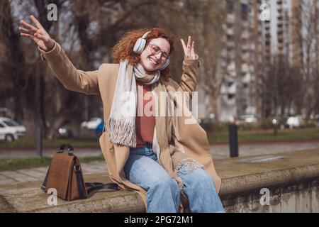 Ritratto naturale di allegra donna zenzero caucasica con lenticelle e capelli ricci. Sta ascoltando musica e godendo il sole. Foto Stock
