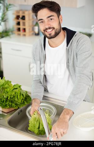 giovane uomo che lava la lattuga nel lavello della cucina Foto Stock