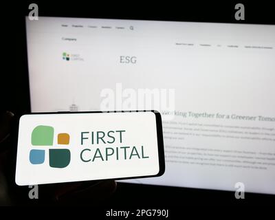 Persona che tiene lo smartphone con il logo della società immobiliare canadese First Capital REIT sullo schermo di fronte al sito Web. Messa a fuoco sul display del telefono. Foto Stock